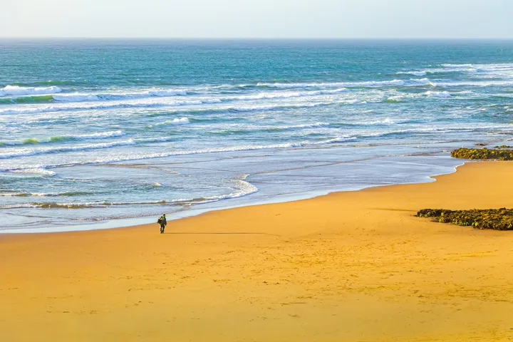 Le pêcheur, Silhouette minuscule sur une grande plage dorée face aux vagues