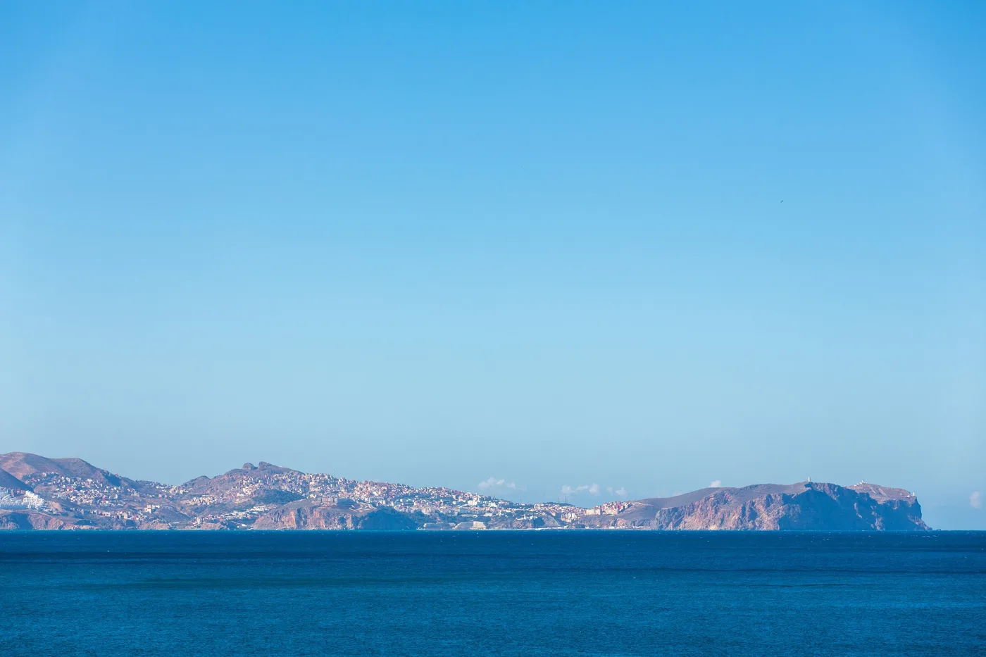 Horizon bleu, Côte lointaine au-dessus d'une mer bleue, ciel dégagé