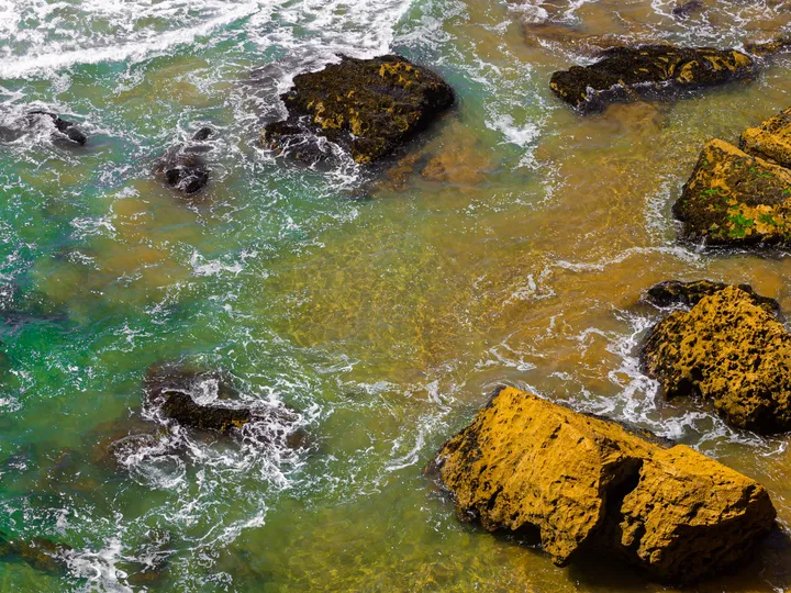 Écume et roche, Eau turquoise et écume autour de rochers dorés vus d'en haut